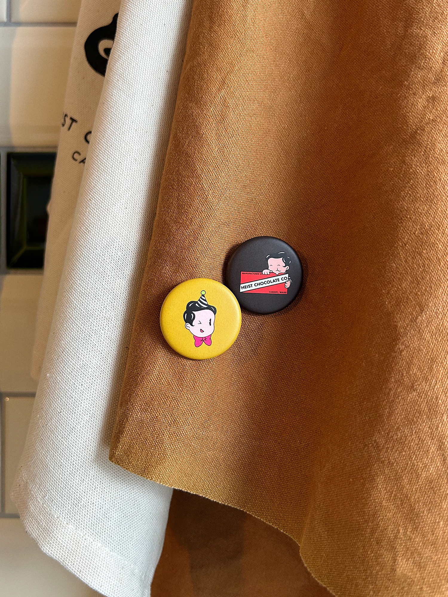 A brown apron with one yellow badge and one brown badge.