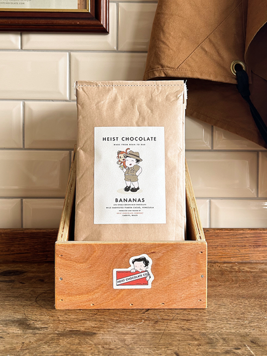 Bar of Heist Chocolate sitting inside a wooden box against a tiled background.