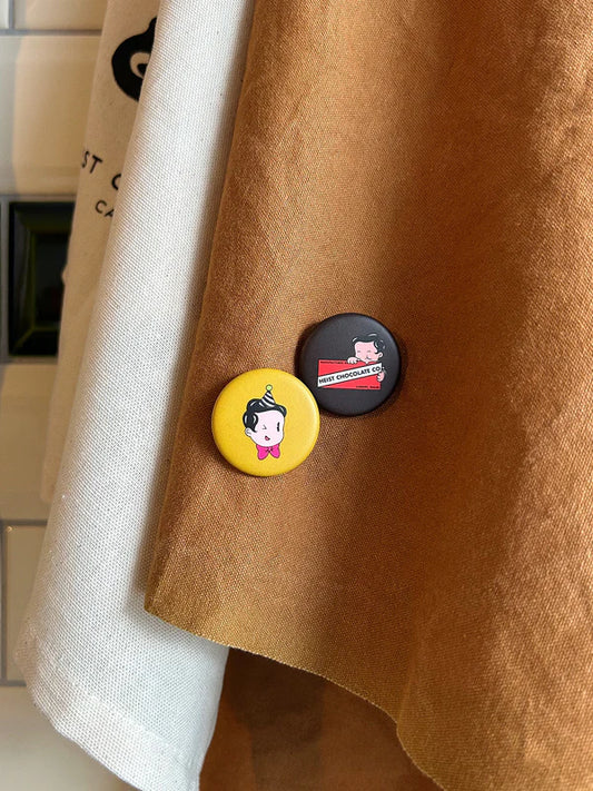 A brown apron with one yellow badge and one brown badge.