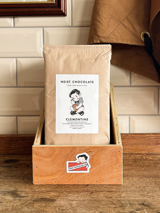 Bar of Heist Chocolate sitting inside a wooden box against a tiled background.