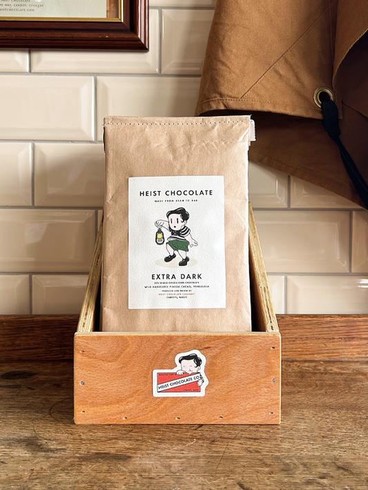 Bar of Heist Chocolate sitting inside a wooden box against a tiled background.