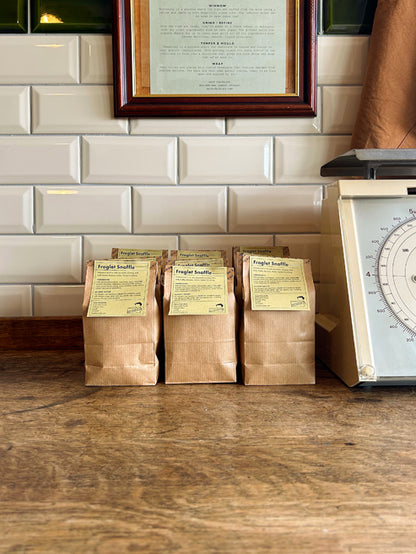 Brown bags with a green label sitting on a wooden table against a tiled background.