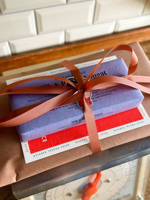 A bundle of Heist chocolate. Wrapped in paper and tied with a ribbon. Sat on some old scales.