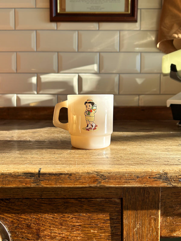 A cream, milk glass mug on a wooden table with the sun shining upon it.