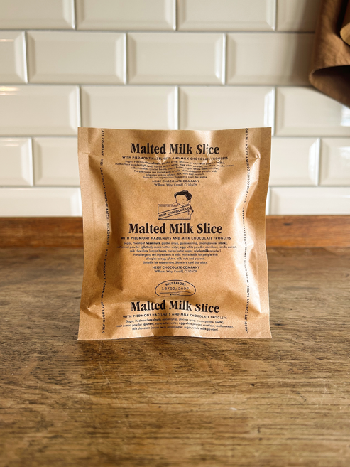 A single packet of a Malted Milk Slice stands upright on a wooden countertop against a white metro tile backsplash.