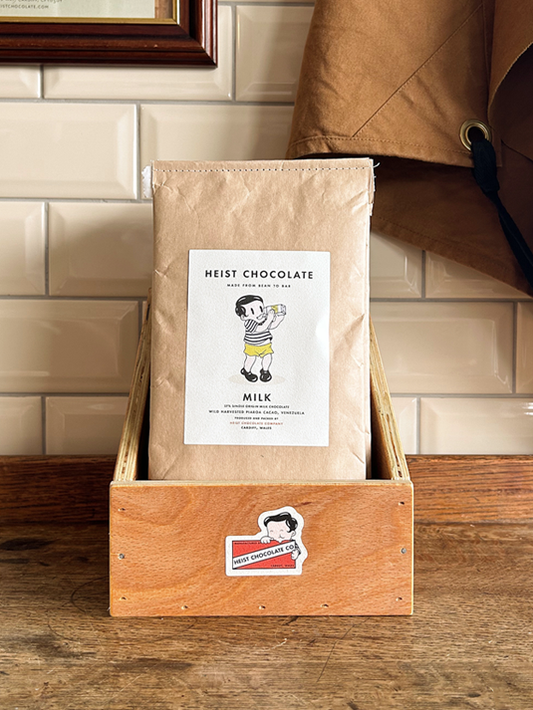 Bar of Heist Chocolate sitting inside a wooden box against a tiled background.