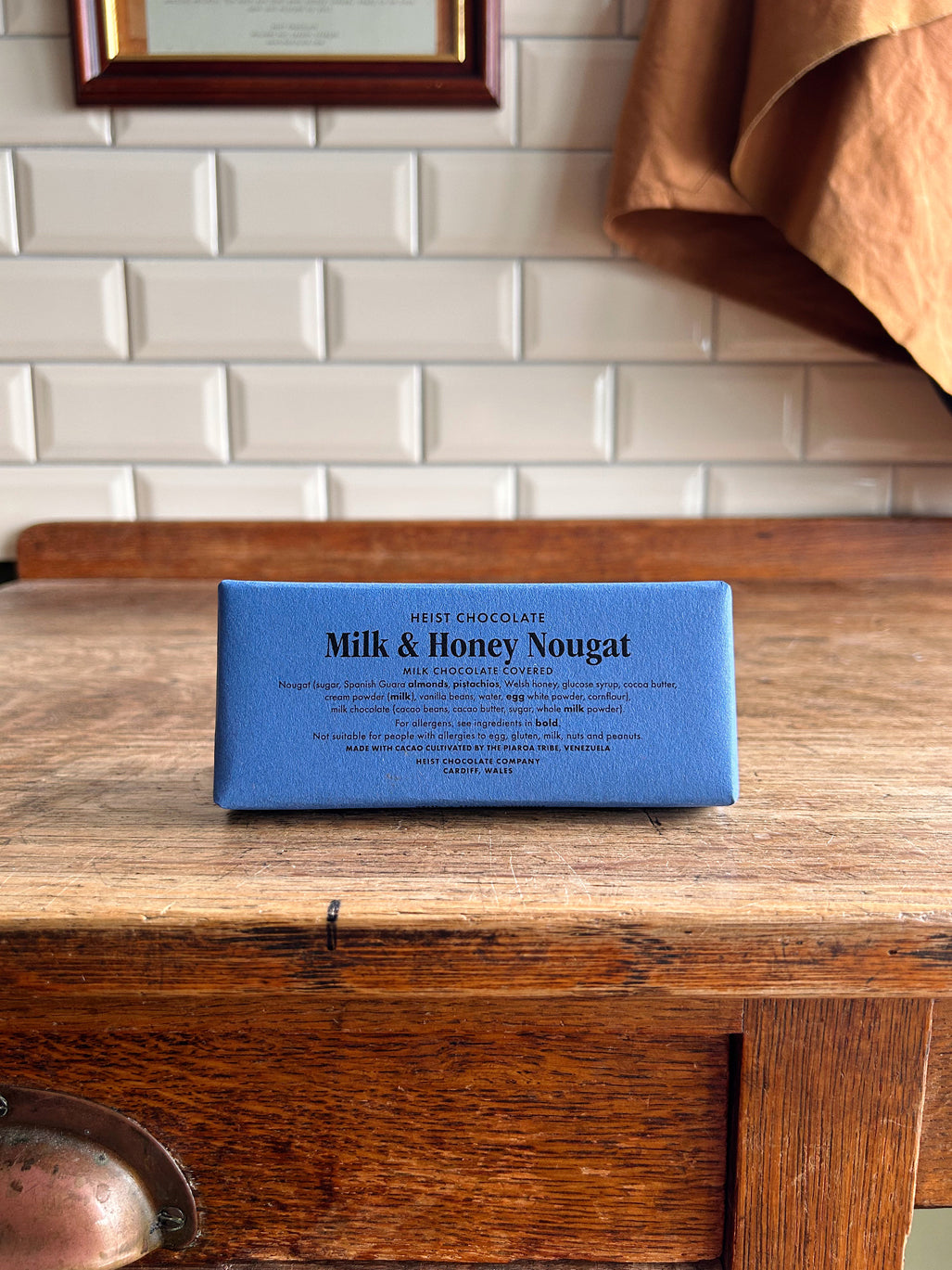 A bean to bar milk chocolate bar in a blue paper wrapper with milk and honey nougat printed on the front in black text.