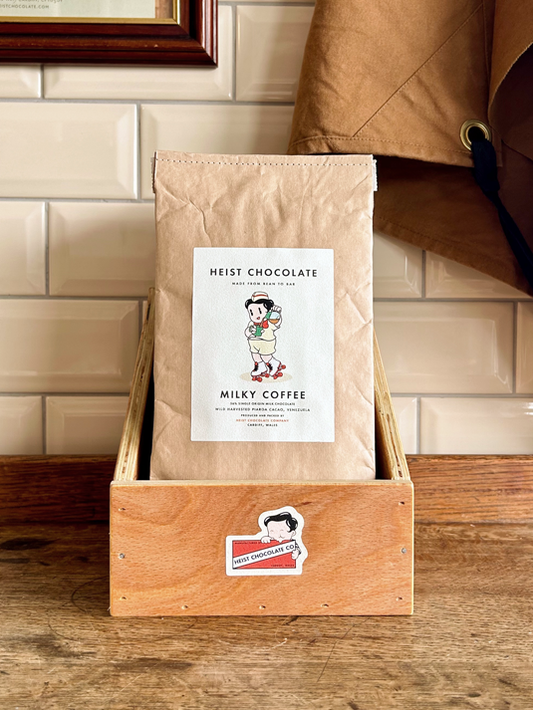 Bar of Heist Chocolate sitting inside a wooden box against a tiled background.