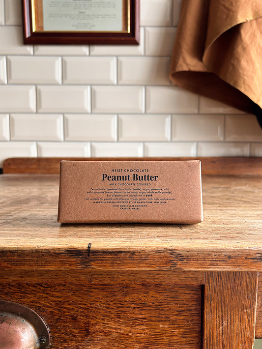 A bean to bar milk chocolate bar in a brown paper wrapper with peanut butter printed on the front in black text.