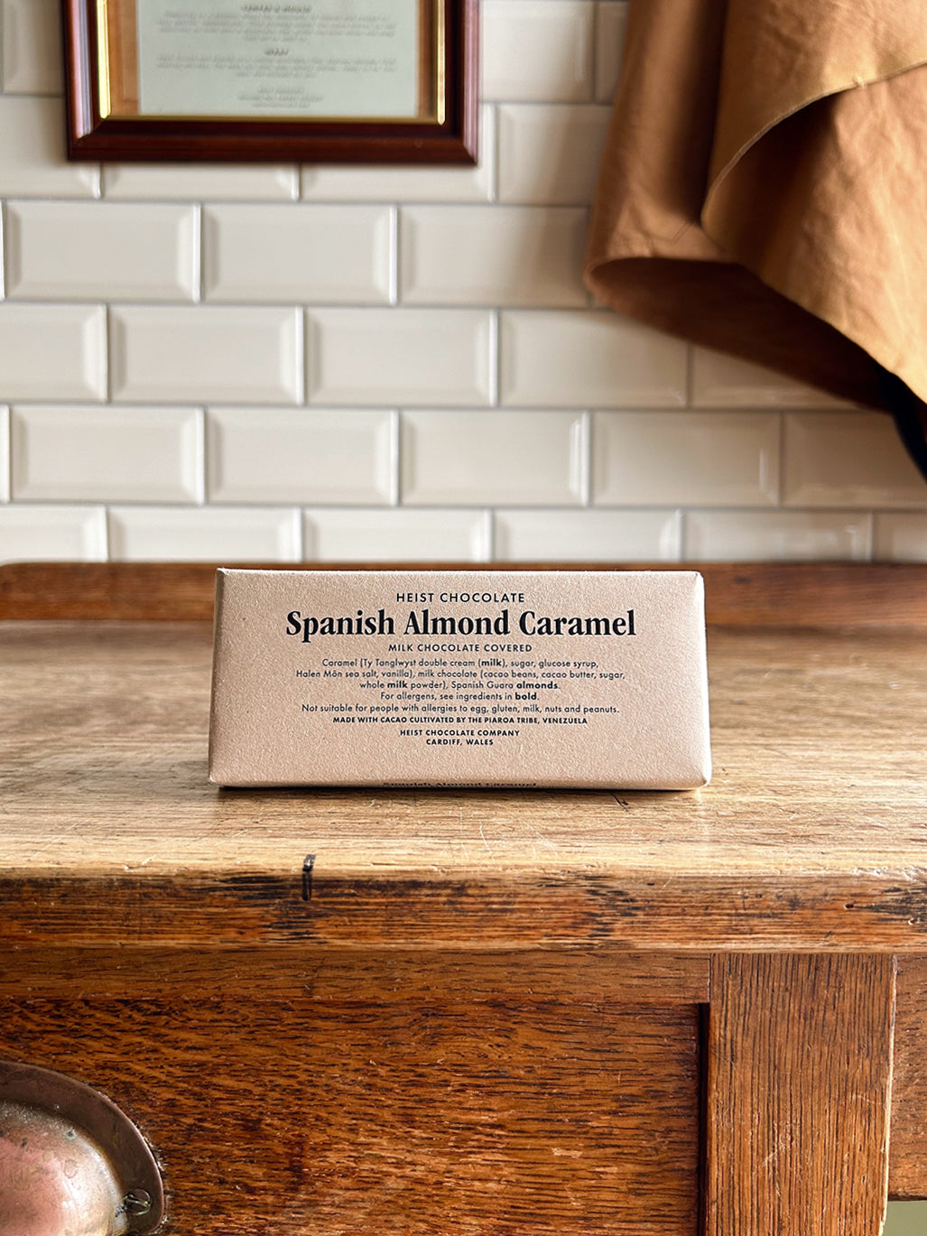 A bean to bar milk chocolate bar in a beige paper wrapper with Spanish Almond Caramel printed on the front in black text.