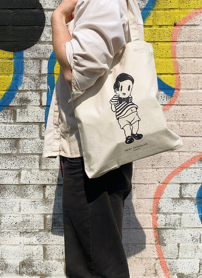 Person wearing black jeans and white shirt holding a tote bag over their shoulder.